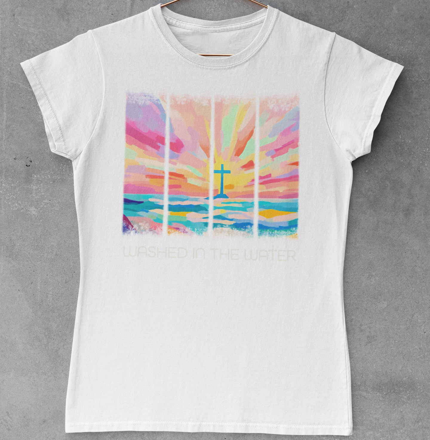 White t-shirt with a colorful cross design on a hanger against a gray concrete wall.
