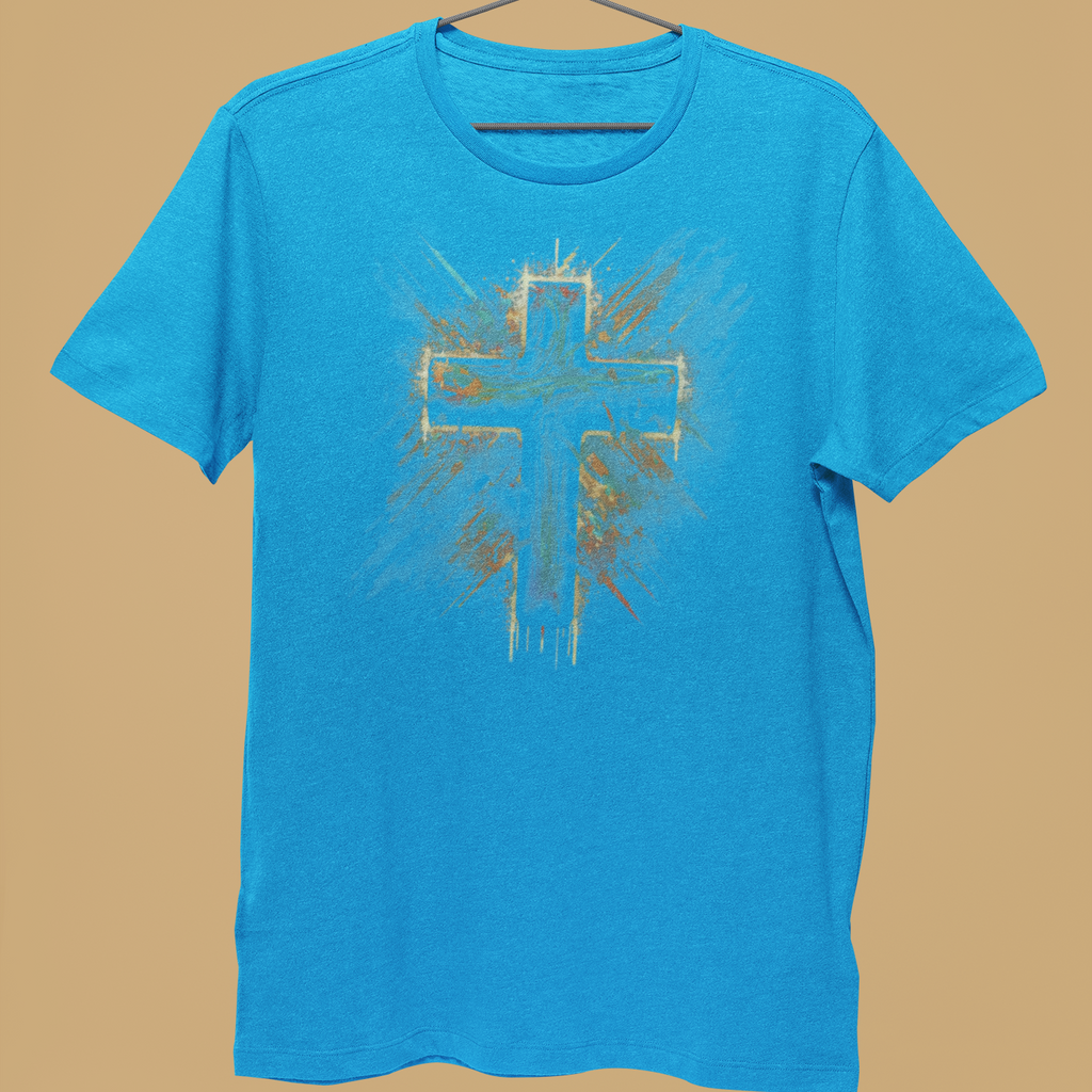 A bright blue short-sleeve t-shirt hanging on a metal hanger, held by a person's hand against a solid tan background. The shirt features a distressed, spray-painted style graphic of a cross in the center with gold and white paint details.