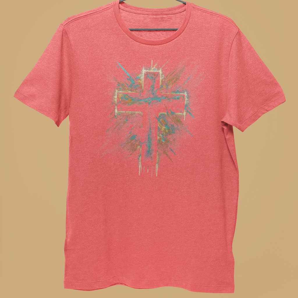 A coral pink heather t-shirt with a colorful cross graphic on the front, hanging on a black wire hanger held by a person's hand against a solid tan background.