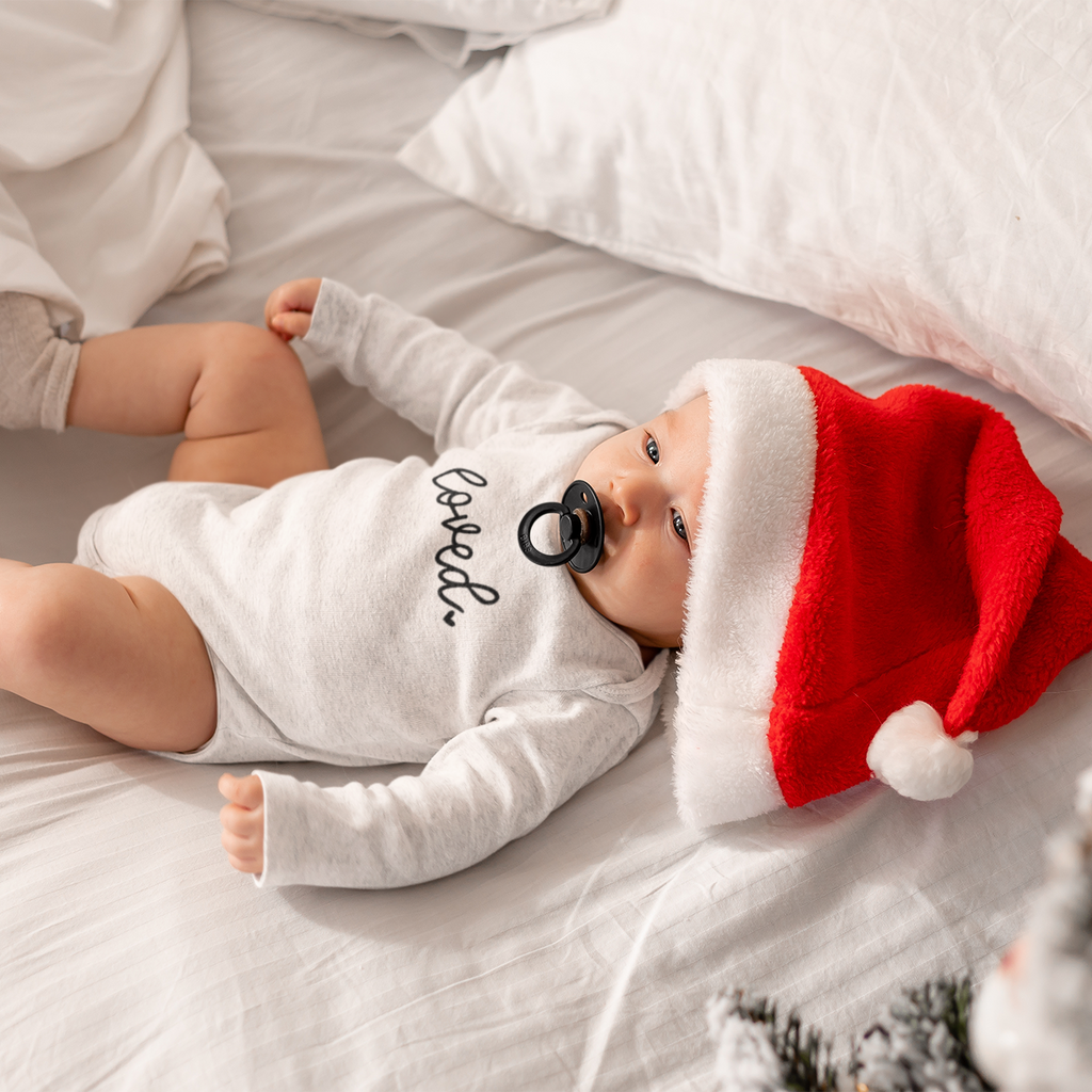Baby on white bedding wearing a white long sleeve Loved baby grow.
