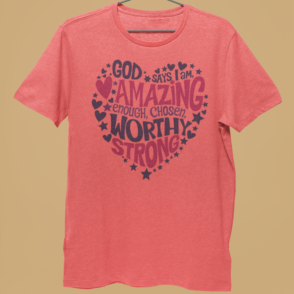 A coral pink heathered t-shirt hanging on a metal hanger held by a person's hand, featuring a dark pink and navy graphic text design on the front, set against a solid tan background.