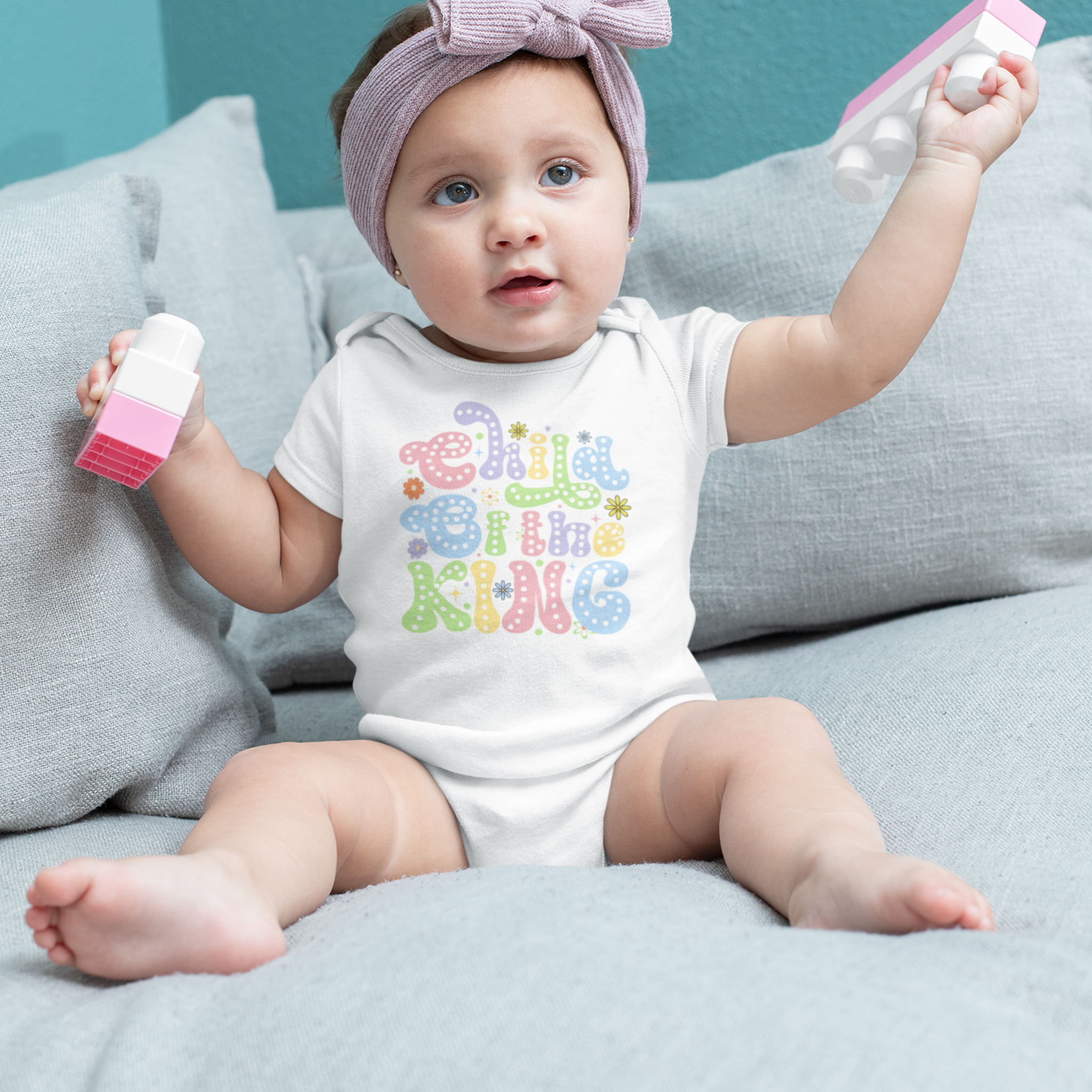 Baby girl on a light blue couch wearing a white short sleeve Child Of The King baby grow.
