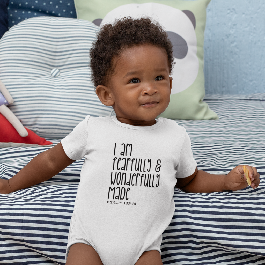 Baby on striped bedding wearing a white short sleeve baby grow printed with I Am Fearfully and Wonderfully Made, Psalm 139:14.