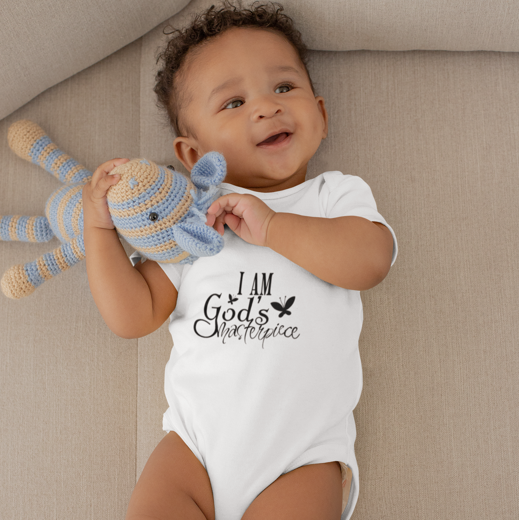 Baby on a beige couch wearing a white short sleeve baby grow printed with I Am God's Masterpiece.