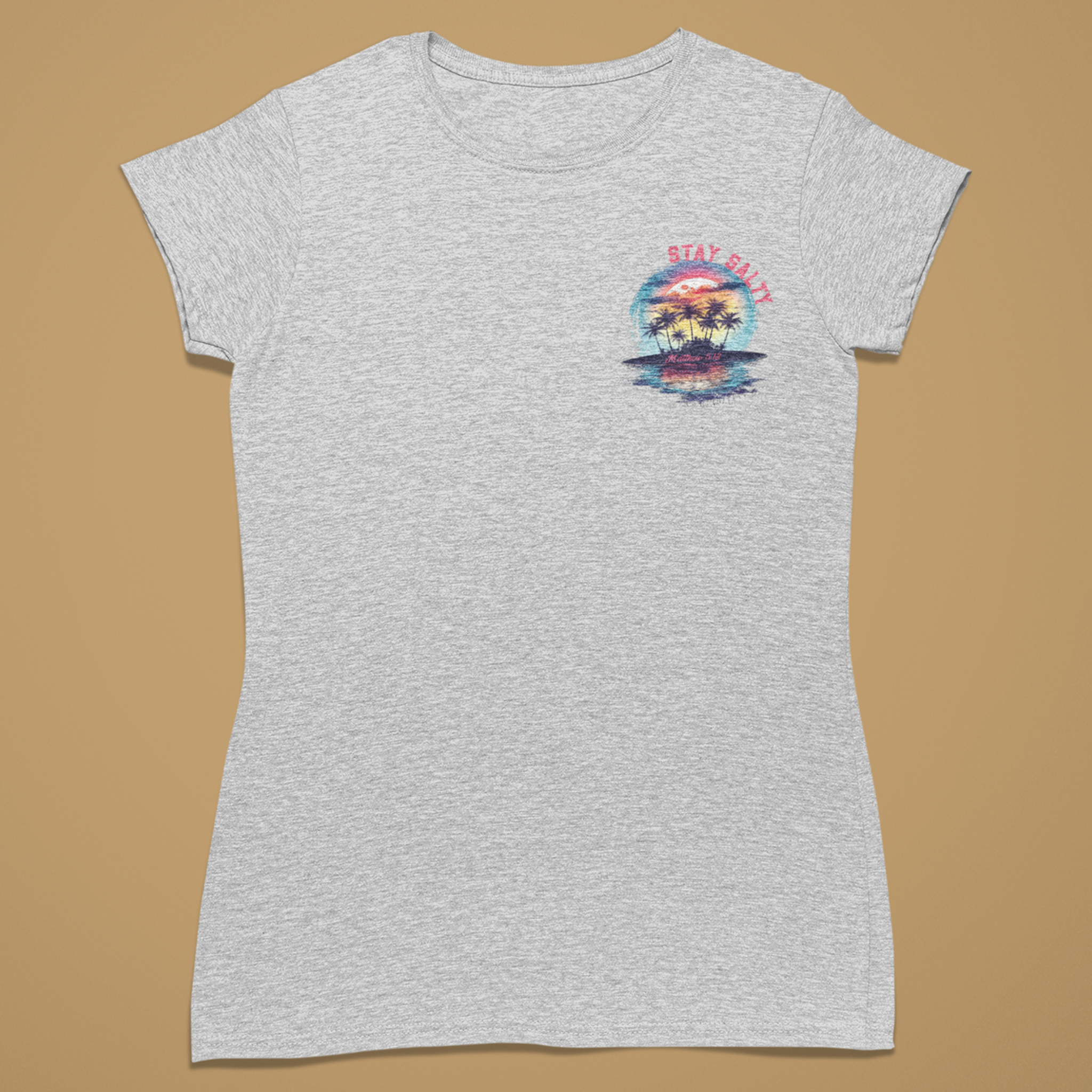 A light heather gray short-sleeve t-shirt with a small multicolor graphic on the left chest depicting a sunset over water with palm trees and the text 'STAY CALM', displayed flat against a solid tan background.